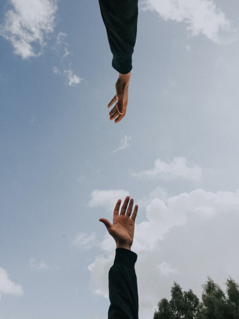 two hands reaching out to each other with sky background signifying mentoring and coaching