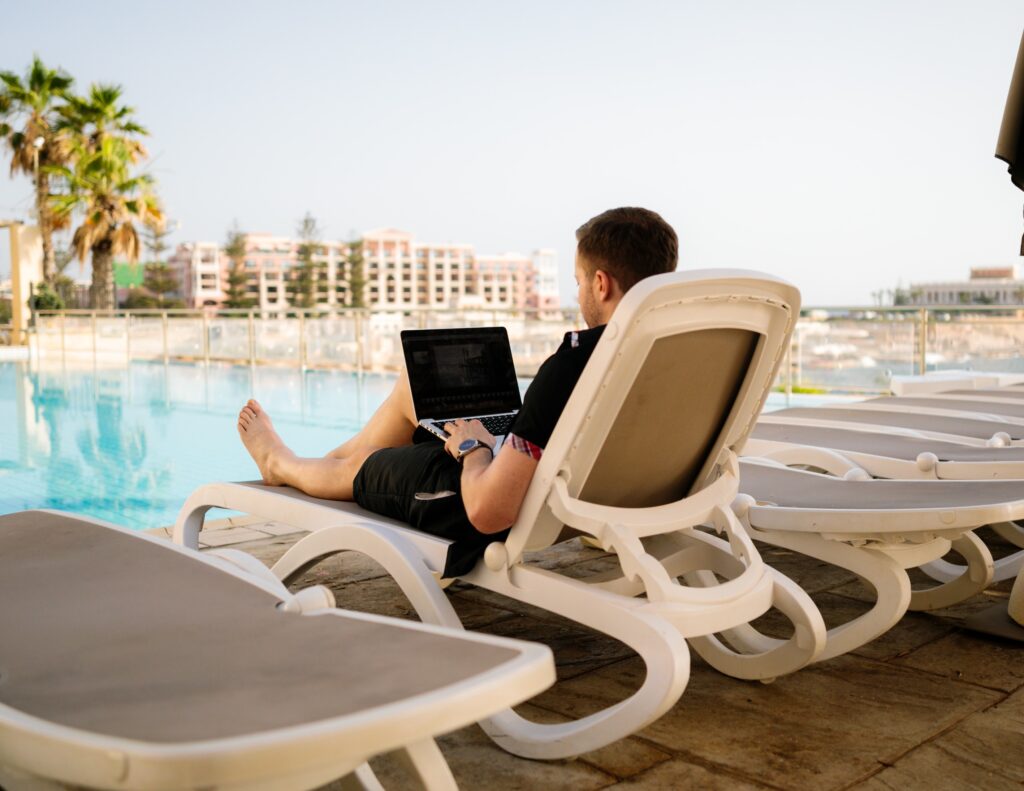 Male digital nomad with laptop working on the bench beside the resort's pool